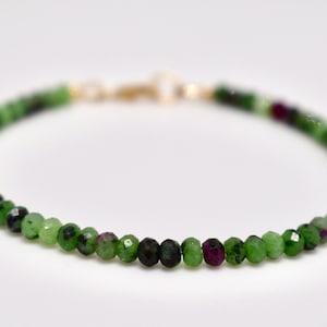 Può includere: Un delicato braccialetto con piccole perline sfaccettate nei toni del verde, verde scuro e amaranto. Le perline sono infilate con una chiusura color oro. Il braccialetto è progettato per essere indossato al polso.