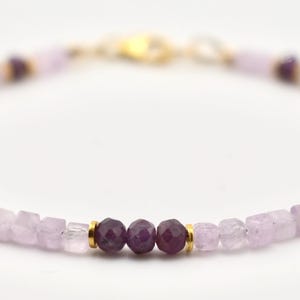 Puede incluir: Delicada pulsera con piedras preciosas de color púrpura claro y púrpura oscuro alternadas. La pulsera tiene un cierre dorado y detalles dorados entre las piedras preciosas. Las piedras son pequeñas y facetadas. Joya ideal para el uso diario.