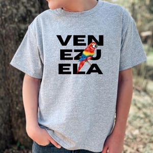 May include: A gray t-shirt with the word "VENEZUELA" printed in black letters. A colorful parrot is perched on the letter "E".