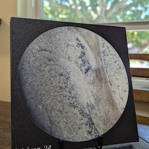 May include: A black canvas print with a circular image of a gray and white textured surface with a brown streak. The text "Erickson, 24" is printed in white at the bottom of the canvas.