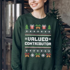 May include: A dark green long-sleeve crewneck sweatshirt featuring a white, red, and green holiday-themed knit pattern. The design includes Christmas trees, gift boxes, bells, and snowflakes, with the text VALUED CONTRIBUTOR in white letters.
