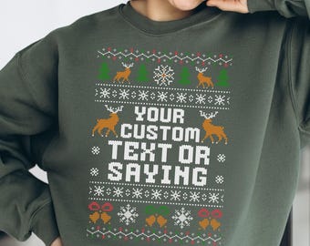 Op de afbeelding: Een olijfgroene sweatshirt met een feestelijk ontwerp. Het ontwerp bevat rendieren, sneeuwvlokken en kerstbomen. De tekst "YOUR CUSTOM TEXT OR SAYING" is in het wit gedrukt. Een vrouw draagt de sweatshirt.