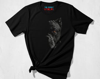 May include: Black t-shirt with a detailed graphic of a dog's face, showing one amber eye. The text "WE PRINT UWEAR" is printed in red and blue on the upper part of the shirt. The shirt is knotted at the bottom.