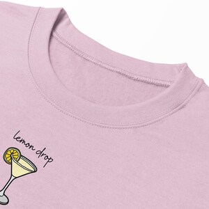 Pu&ograve; includere: Una felpa rosa con una grafica di un cocktail al limone e il testo "lemon drop" in nero.