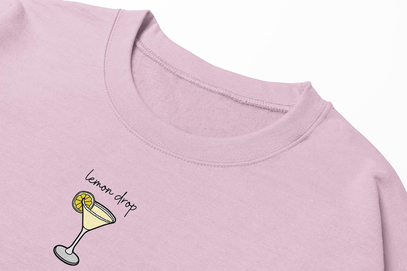 Pu&ograve; includere: Una felpa rosa con una grafica di un cocktail al limone e il testo "lemon drop" in nero.