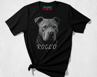 May include: Black t-shirt with a detailed grayscale illustration of a dog's face, and the name "ROCKO" in white script below. The shirt also has the text "WE PRINT UWEAR:" at the top.