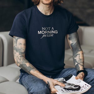 Pu&ograve; includere: Una t-shirt blu navy con la scritta "NOT A MORNING person" stampata in bianco sul davanti.