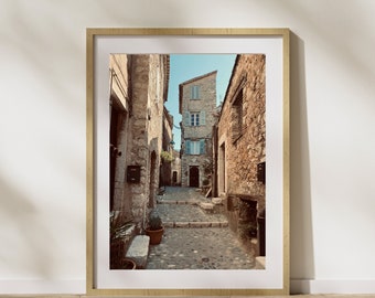 Puede incluir: Una calle estrecha y adoquinada en un pueblo europeo con edificios de piedra a ambos lados. Los edificios son antiguos y tienen un encanto rústico. La calle está vacía y el sol brilla.