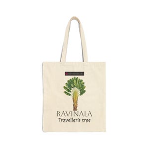May include: A beige canvas tote bag featuring a graphic of a green traveller's tree. Above the tree is a small dark rectangular logo with the text KRYSTAHLINE. Below the tree, the text RAVINALA and Traveller's tree are printed in black.