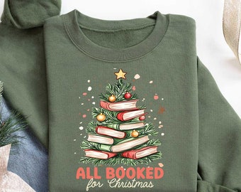 May include: A green sweatshirt with a Christmas tree design made of stacked books. The text "All Booked for Christmas" is printed below the tree.