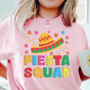 May include: Pink t-shirt with a colorful graphic of a sombrero and the text "Fiesta Squad".