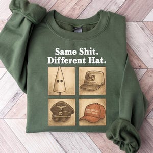 May include: Green sweatshirt with the text "Same Shit. Different Hat." and four hat illustrations. The illustrations include a white hood, a tan hat, a black hat, and a red baseball cap.