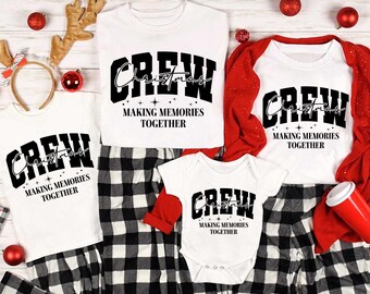May include: A set of four white t-shirts with black text that reads "CREW Christmas Making Memories Together". The shirts are paired with black and white plaid pants. The shirts are arranged on a white wooden surface with red ornaments.