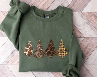 May include: A green sweatshirt with a festive design of four Christmas trees. Each tree is decorated with a different pattern: plaid, leopard print, pine cones, and a star on top.