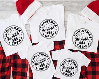 May include: A set of five white t-shirts with a black Christmas design featuring Santa Claus in a sleigh with reindeer. The design includes the text "Christmas Crew". The shirts are paired with red and black plaid pants.