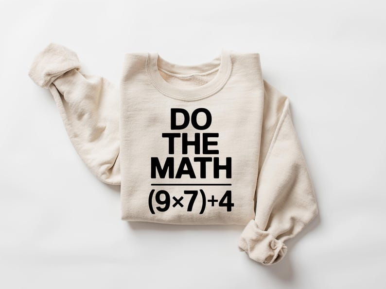 May include: A cream-colored sweatshirt with the text "DO THE MATH" in bold black letters. Below the text is the equation (9x7)+4. The sweatshirt is folded with the sleeves rolled up.