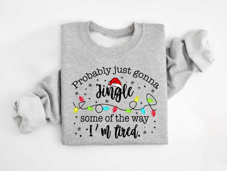 Peut inclure: Un sweat-shirt gris clair avec le texte "Probably just gonna Jingle some of the way. I'm tired." Le mot "Jingle" est surmont&eacute; d'un bonnet de P&egrave;re No&euml;l et entour&eacute; de guirlandes lumineuses.