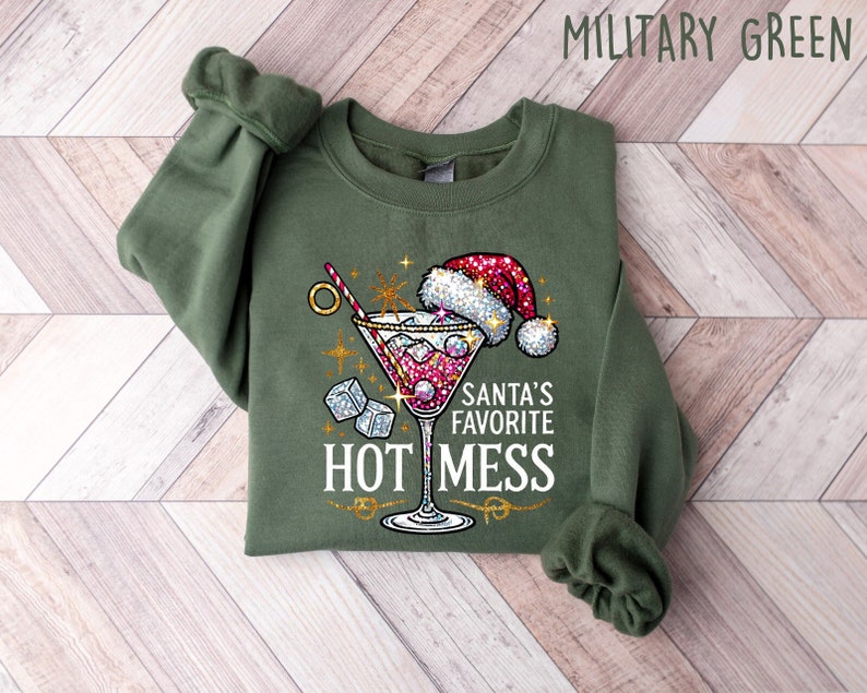 May include: A green sweatshirt with a glittery design of a martini glass with a Santa hat on top. The text "Santa's Favorite Hot Mess" is printed below the glass.