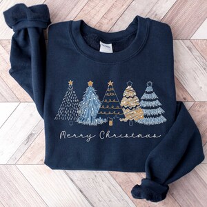 May include: A navy blue sweatshirt with a festive design of four stylized Christmas trees in gold and blue with the text "Merry Christmas" underneath.