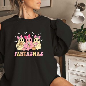 May include: Black sweatshirt with a graphic of three ghosts wearing pink bows and holding pumpkins. The text "PANTASMAS" is printed below the ghosts.
