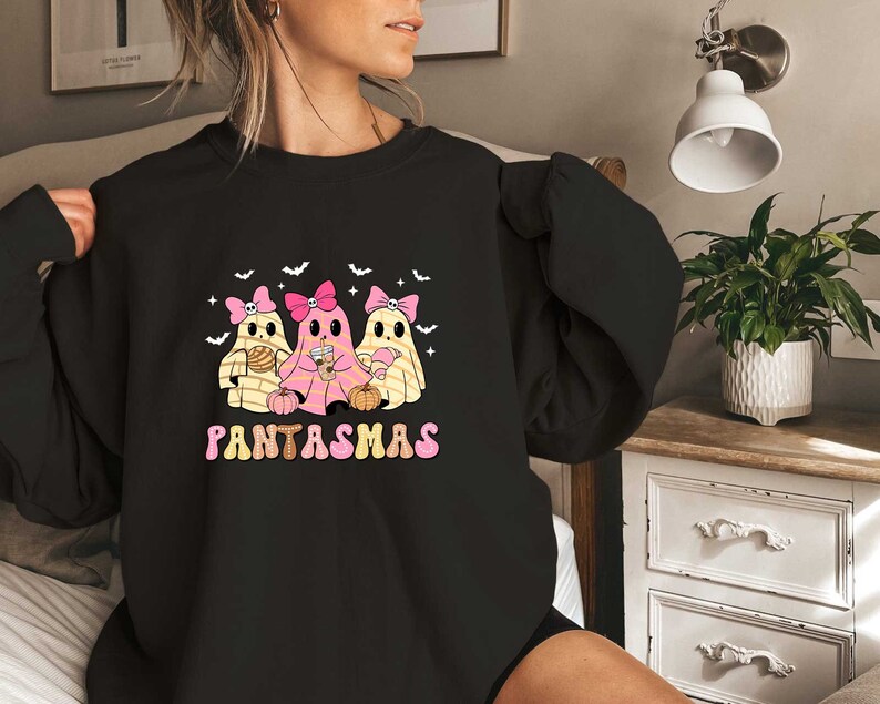 May include: Black sweatshirt with a graphic of three ghosts wearing pink bows and holding pumpkins. The text "PANTASMAS" is printed below the ghosts.