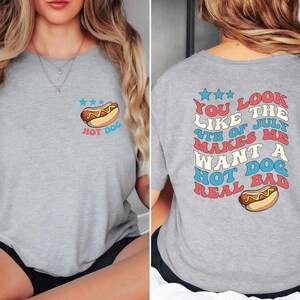Puede incluir: Camiseta gris con un gr&aacute;fico de un hot dog en la parte delantera y el texto "You look like the 4th of July makes me want a hot dog real bad" en la parte posterior.