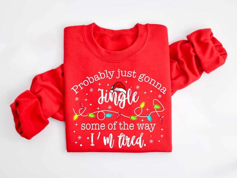 Peut inclure: Sweat-shirt rouge avec le texte "Probably just gonna jingle some of the way, I'm tired." Le motif comprend un bonnet de P&egrave;re No&euml;l, des guirlandes lumineuses et des flocons de neige. V&ecirc;tement de f&ecirc;te sur le th&egrave;me des f&ecirc;tes.