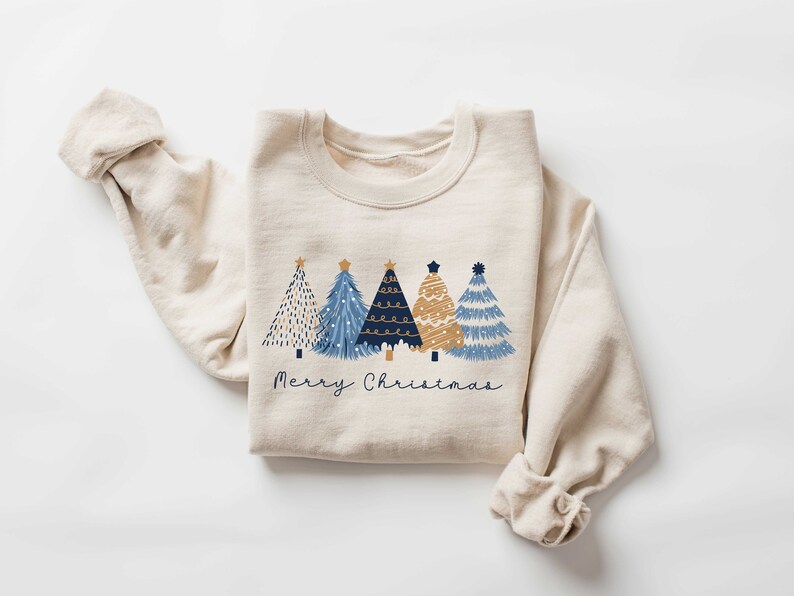 May include: A beige sweatshirt with a graphic of four blue and gold Christmas trees and the text "Merry Christmas".