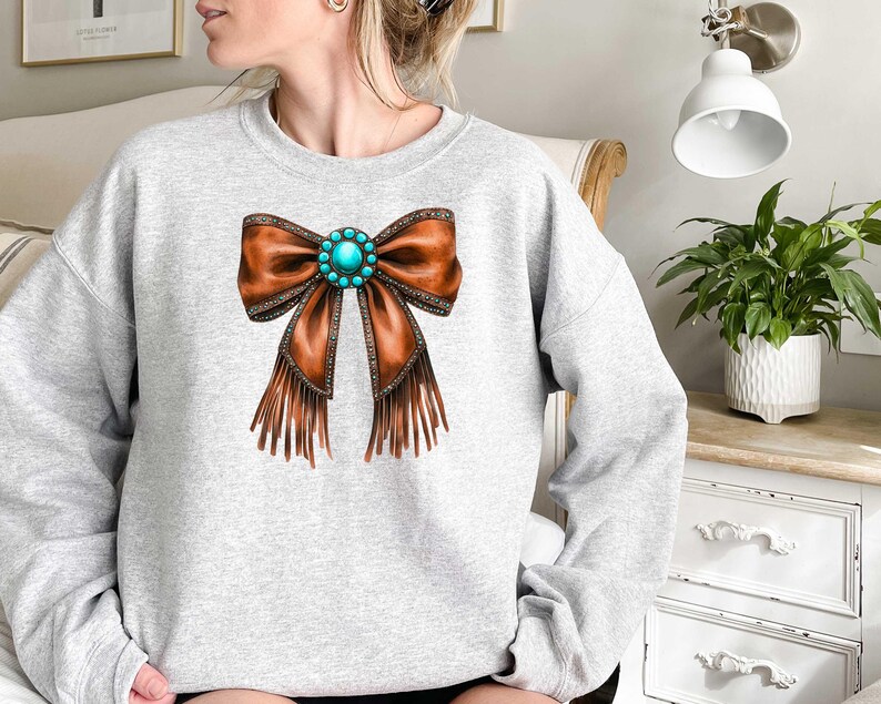May include: A gray sweatshirt with a brown leather bow with turquoise gemstone embellishment and fringe detail.