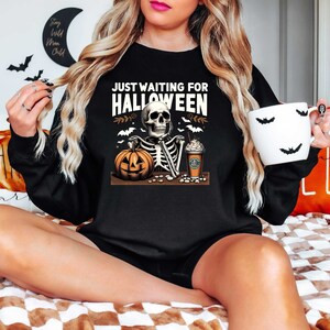 May include: Black sweatshirt with a skeleton holding a pumpkin and a coffee cup. The text on the sweatshirt reads "Just Waiting for Halloween".
