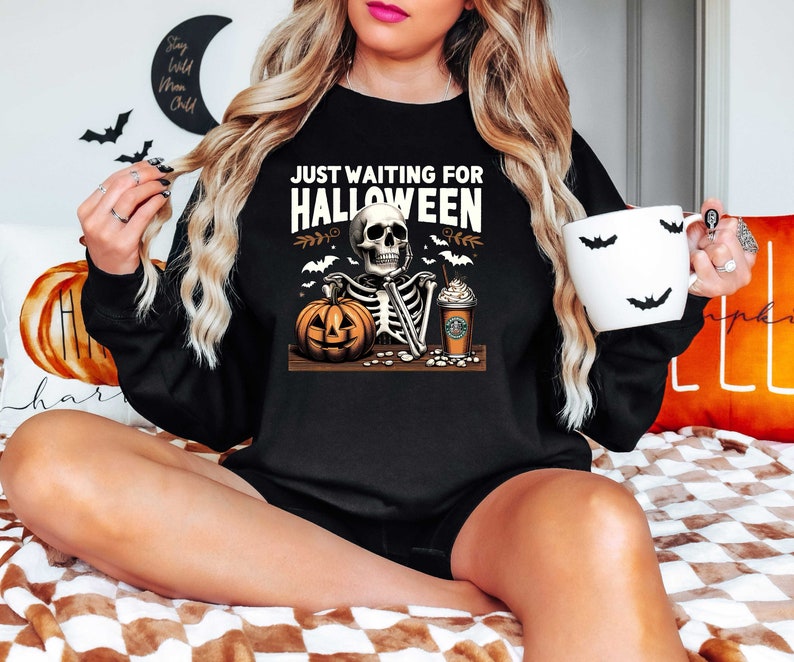 May include: Black sweatshirt with a skeleton holding a pumpkin and a coffee cup. The text on the sweatshirt reads "Just Waiting for Halloween".