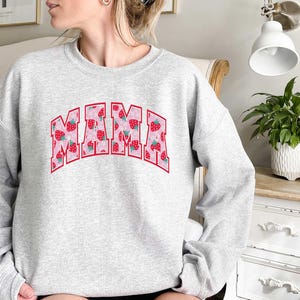 May include: Gray sweatshirt with the word "MAMA" printed in pink letters with a strawberry pattern. The letters are outlined in red.