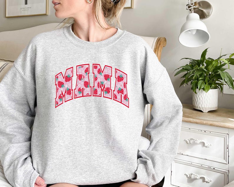 May include: Gray sweatshirt with the word "MAMA" printed in pink letters with a strawberry pattern. The letters are outlined in red.