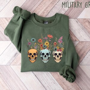 May include: A green sweatshirt with a floral skull design. The skulls are wearing a crown of flowers in shades of pink, yellow, and blue.