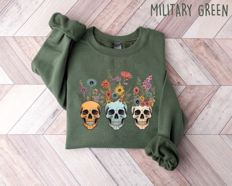May include: A green sweatshirt with a floral skull design. The skulls are wearing a crown of flowers in shades of pink, yellow, and blue.