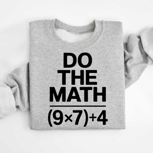 May include: A light gray sweatshirt with the text "DO THE MATH" in bold black letters. Below the text is the equation (9x7)+4. The sweatshirt has long sleeves.
