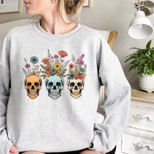 May include: Gray sweatshirt with a floral skull design. The skulls are yellow, blue, and green with colorful flowers on top.