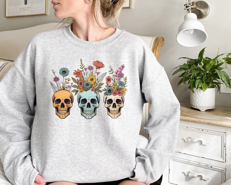 May include: Gray sweatshirt with a floral skull design. The skulls are yellow, blue, and green with colorful flowers on top.