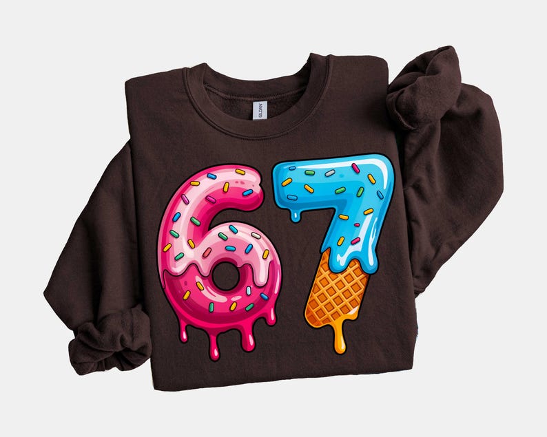 May include: A dark brown sweatshirt featuring a colorful graphic of the number "67". The "6" is designed as a pink donut with sprinkles, and the "7" is blue with a waffle cone base. The design has a dripping effect.