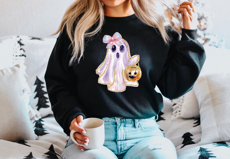 May include: Black sweatshirt featuring a watercolor ghost with a bow and a jack-o'-lantern. The ghost is white and lavender with gold glitter accents. The jack-o'-lantern is orange and gold. A fun Halloween-themed design.