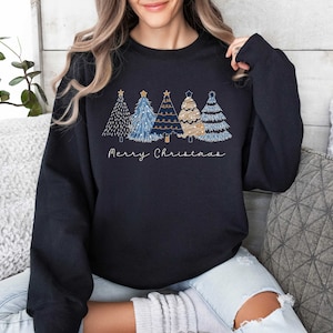 May include: A black sweatshirt with a festive design of four stylized Christmas trees in shades of blue and gold. The trees are decorated with stars and lights. The text "Merry Christmas" is printed below the trees.