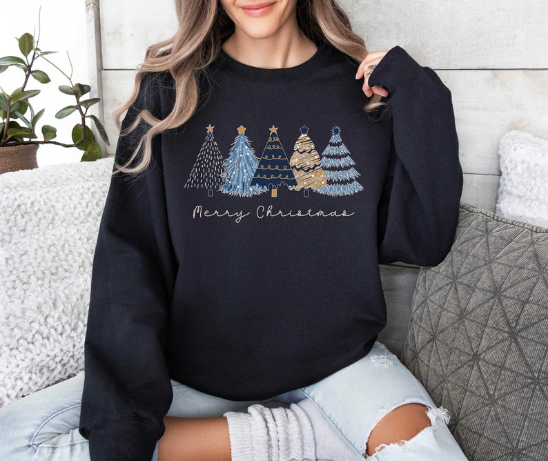 May include: A black sweatshirt with a festive design of four stylized Christmas trees in shades of blue and gold. The trees are decorated with stars and lights. The text "Merry Christmas" is printed below the trees.