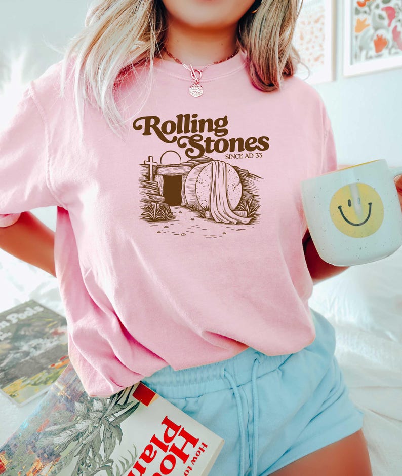 May include: Pink t-shirt with a brown graphic of a tomb with the text "Rolling Stones Since AD 33".