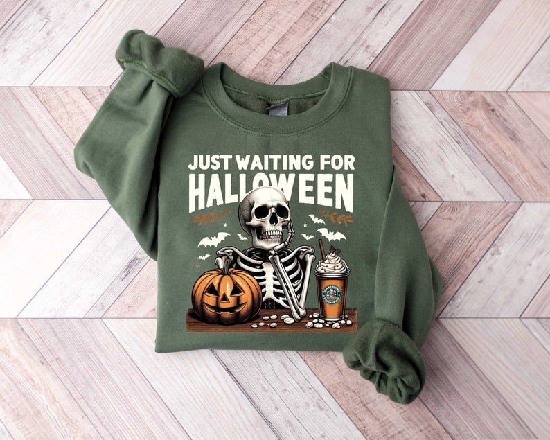 May include: Green sweatshirt with a skeleton holding a pumpkin and a coffee cup. The text "Just Waiting for Halloween" is printed on the front.