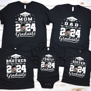 Puede incluir: Un conjunto de camisetas negras y un body, cada uno con un gr&aacute;fico blanco. Las camisetas y el body muestran los textos "Proud Mom", "Dad", "Brother", "Family" y "Sister" con "Of a Class of 2024 Graduate" y una foto.