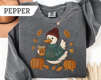 May include: Pepper-colored sweatshirt featuring an embroidered duck wearing a hat, scarf, and boots, holding a coffee cup, and walking past pumpkins and fall leaves. The word "PEPPER" is in a white rectangle in the upper left corner.