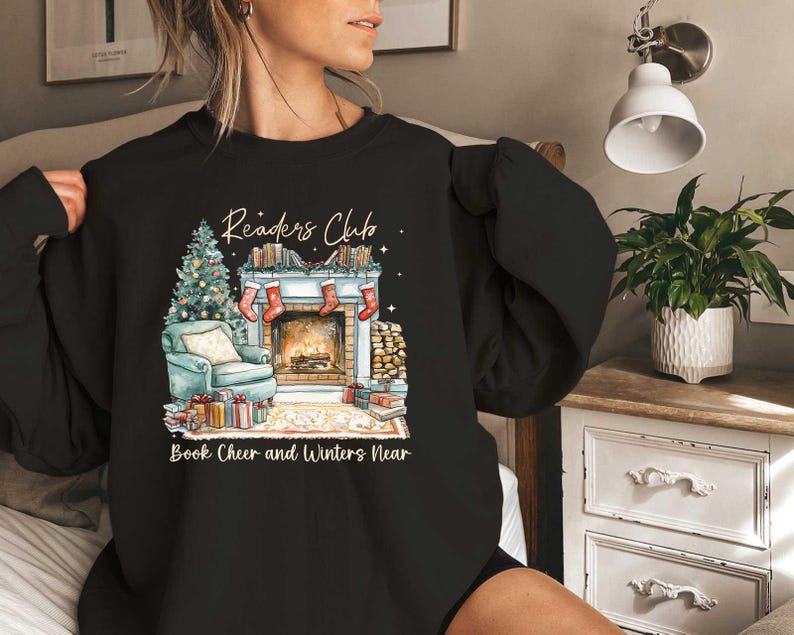K&ouml;nnte beinhalten: Schwarzes Sweatshirt mit einem Grafikdruck eines Kamins, B&uuml;chern und eines Weihnachtsbaums. Der Text "Readers Club" befindet sich &uuml;ber dem Grafikdruck und "Book Cheer and Winters Near" darunter.