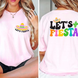 May include: Pink t-shirt with a small sombrero and the text "Let's Fiesta" on the front. The back of the shirt has the text "Let's Fiesta" in rainbow colors with a green cactus.