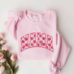 May include: Pink sweatshirt with a strawberry print and the word "MAMA" in red letters.