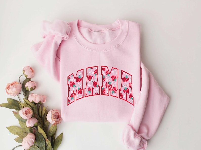 May include: Pink sweatshirt with a strawberry print and the word "MAMA" in red letters.